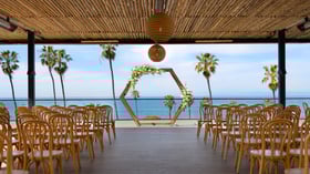 Wedding ceremony space with geometric floral arch and bentwood chairs facing ocean view