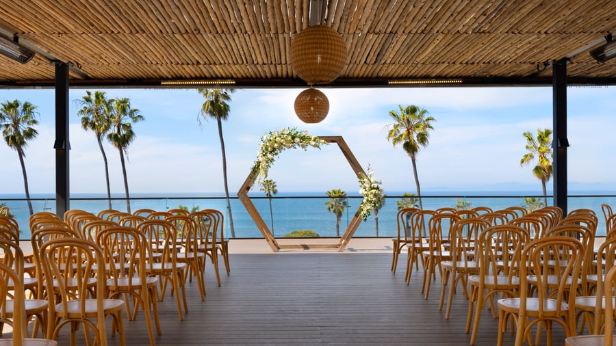 Wedding ceremony space with geometric floral arch and bentwood chairs facing ocean view