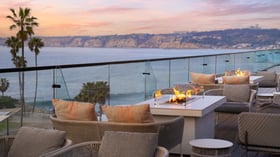 Fire pit lounge area with wicker seating and ocean sunset backdrop
