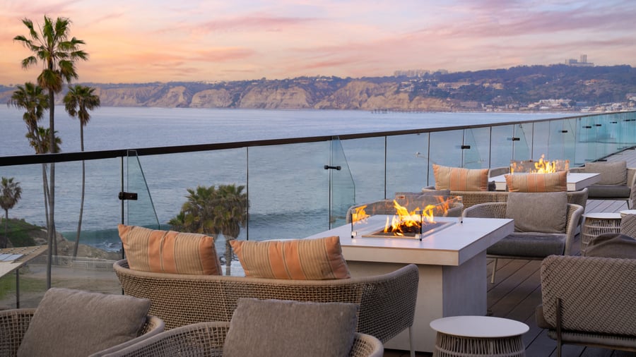 Fire pit lounge area with wicker seating and ocean sunset backdrop