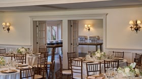 Reception space at The Barker House showing elegant dining tables and buffet area with chafing dishes, white florals, and wall sconces.