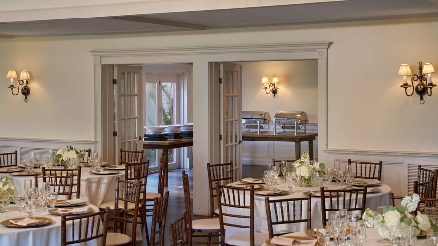 Reception space at The Barker House showing elegant dining tables and buffet area with chafing dishes, white florals, and wall sconces.