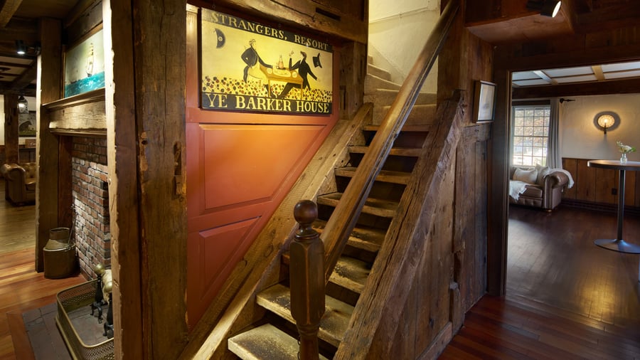 Rustic interior of The Barker House featuring an antique wooden staircase, exposed beams, vintage signage, and cozy lounge with leather seating.