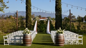 Outdoor wedding ceremony at Bel Vino Winery in Temecula featuring white chairs, wine barrel florals, and vineyard backdrop.