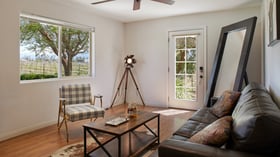 Stylish groom’s suite at Bel Vino Winery with leather sofa, plaid chair, and vineyard view window.
