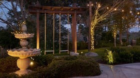 Stone fountain and swing illuminated with string lights at Bel Vino Winery cocktail patio during an evening wedding.