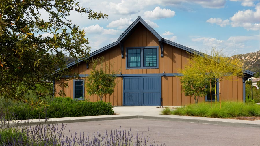 Aerial view of Canopy Grove’s ceremony lawn with wooden chairs arranged around a decorated archway.xterior view of Canopy Grove’s barn with brown siding, blue trim, and surrounding natural landscaping in Escondido, CA.