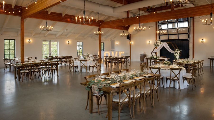 Elegant barn wedding reception with wood tables, greenery centerpieces, and glowing chandeliers at Canopy Grove in Escondido, CA.