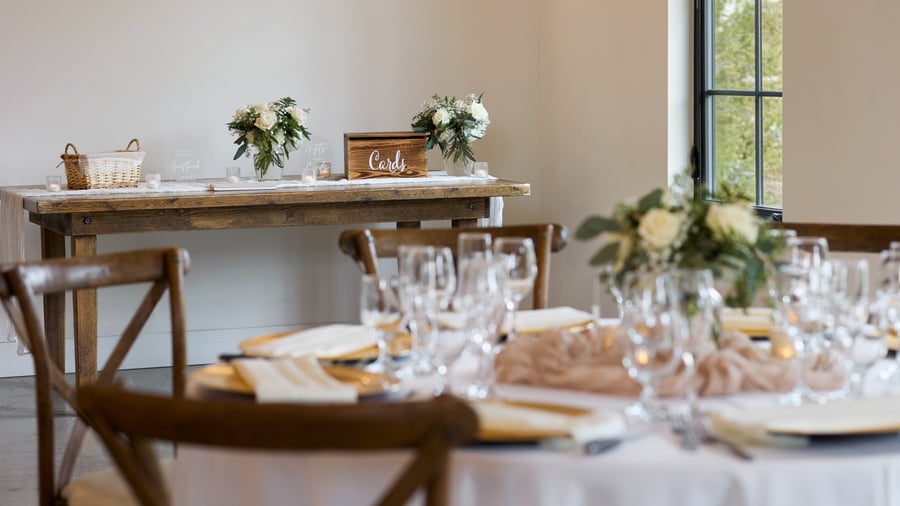 Rustic wood gift and card table decorated with floral arrangements, candles, and signage inside the Canopy Grove wedding reception barn in Escondido, CA.