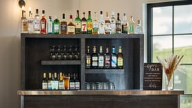Reception bar with liquor display, open bar sign, and signature cocktails at Canopy Grove wedding barn.