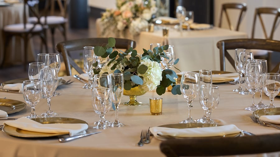 Carlsbad Windmill Loft wedding reception centerpiece with white hydrangeas, greenery, and gold accents.