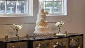 Close-up of elegant white and gold wedding cake at Carlsbad Windmill Loft with floral accents.