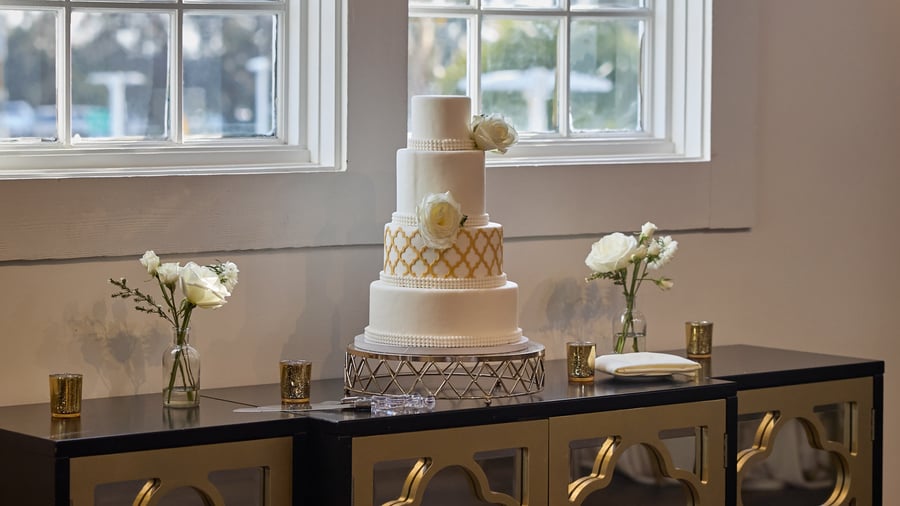 Close-up of elegant white and gold wedding cake at Carlsbad Windmill Loft with floral accents.