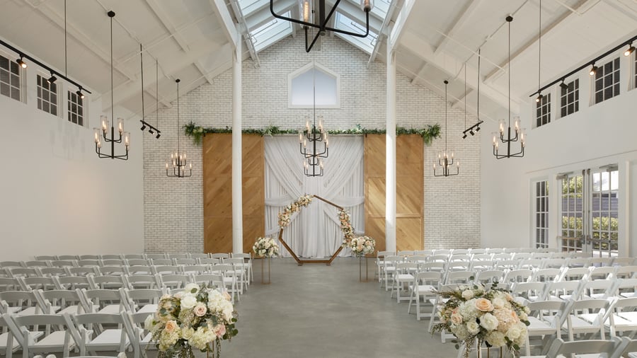 Bright Carlsbad Windmill chapel wedding ceremony with floral hexagon arch and white chairs.