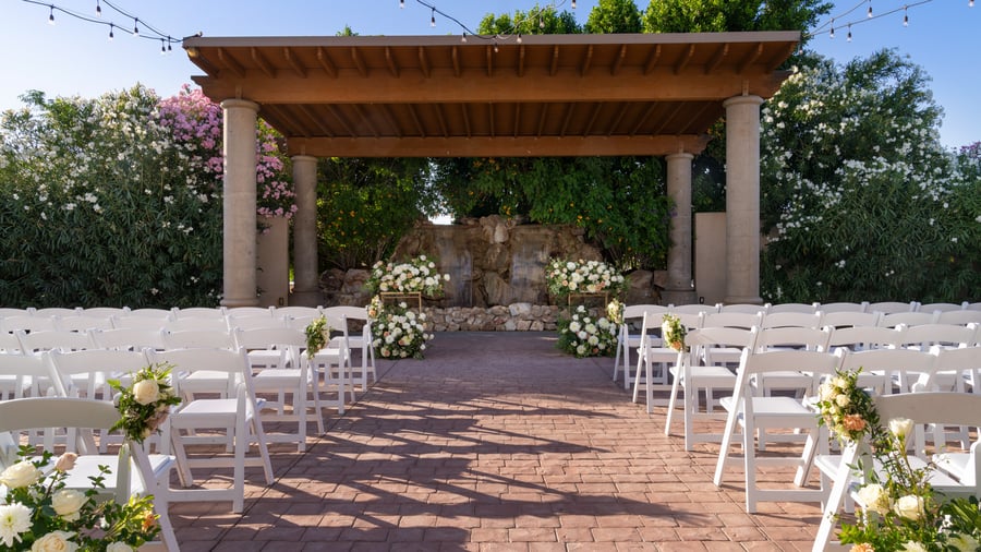 Romantic outdoor wedding ceremony setup at Colby Falls in Arizona featuring a stone waterfall backdrop, white chairs, and floral aisle décor.