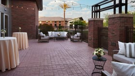 Patio cocktail hour space at Colby Falls Arizona with string lights, lounge seating, high-top tables, and brick exterior walls.
