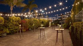 Romantic evening atmosphere in the Garden Courtyard at Cuvier Club by Wedgewood Weddings with bistro lights, cocktail tables, and lush tropical gardens in La Jolla