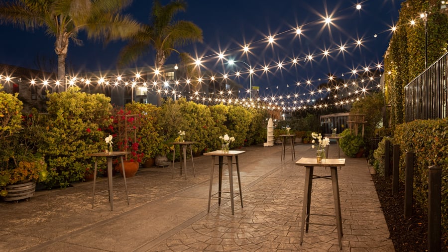 Romantic evening atmosphere in the Garden Courtyard at Cuvier Club by Wedgewood Weddings with bistro lights, cocktail tables, and lush tropical gardens in La Jolla