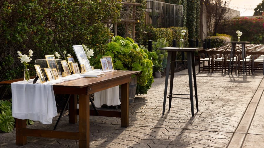 Elegant memory table display in the Garden Courtyard at Cuvier Club by Wedgewood Weddings featuring gold-framed photos, white floral arrangements, and rustic wooden table for La Jolla weddings