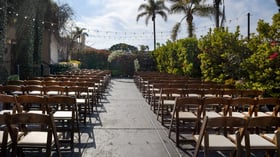 Garden Courtyard ceremony aisle at Cuvier Club by Wedgewood Weddings with wooden cross-back chairs, tropical landscaping, and string lights in La Jolla, California