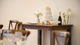 Beautiful three-tier white wedding cake display at Cuvier Club featuring textured buttercream design, champagne flutes, white floral arrangements, and rustic wooden table