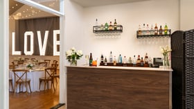 Full-service wedding reception bar at Cuvier Club by Wedgewood Weddings with walnut bar, premium spirits, glassware display, and view into illuminated LOVE sign reception hall