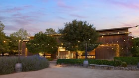 Stunning twilight view of Galway Downs rustic wedding venue featuring wooden barn architecture, twinkling string lights, purple sunset skies, and lavender landscaping in Temecula wine country