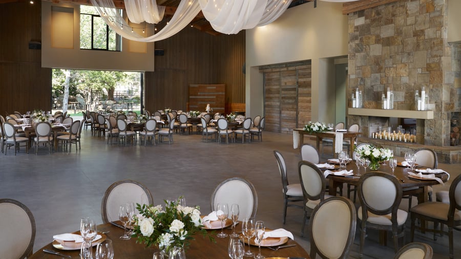 Spectacular grand reception hall at Galway Downs featuring dramatic draped ceiling with twinkling lights, exposed wooden beams, stone fireplace, elegant round tables, and panoramic garden views in Temecula, California