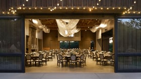 Elegant evening reception at Galway Downs viewed through open barn doors, showcasing draped ceiling lighting, round tables with neutral linens, and warm interior ambiance perfect for Temecula weddings