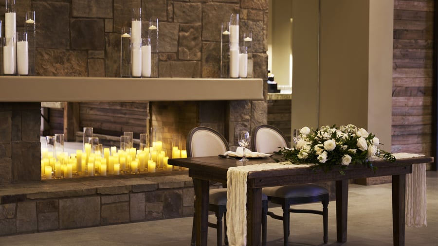 Intimate sweetheart table setup in Galway Downs Wedding Suites featuring a grand stone fireplace, romantic candle displays, and elegant floral arrangements for bride and groom dining