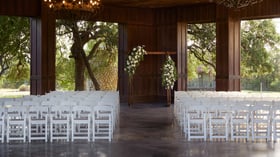 Wedding ceremony inside the Meadow Pavilion at Hofmann Ranch, featuring white seating, floral arch décor, rustic chandeliers, and countryside views through open walls.