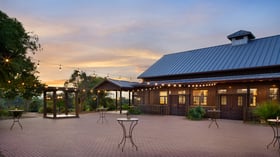 The brick patio at Hofmann Ranch during cocktail hour, featuring string lights, cocktail tables, and a rustic barn backdrop at sunset.