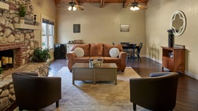 Groom’s suite at the Hofmann Ranch Farm House with a cozy stone fireplace, leather sofa, and rustic wood décor.