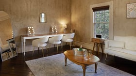 Bridal suite at Hofmann Ranch featuring makeup vanities with lit mirrors, elegant seating, and natural light for wedding preparations.