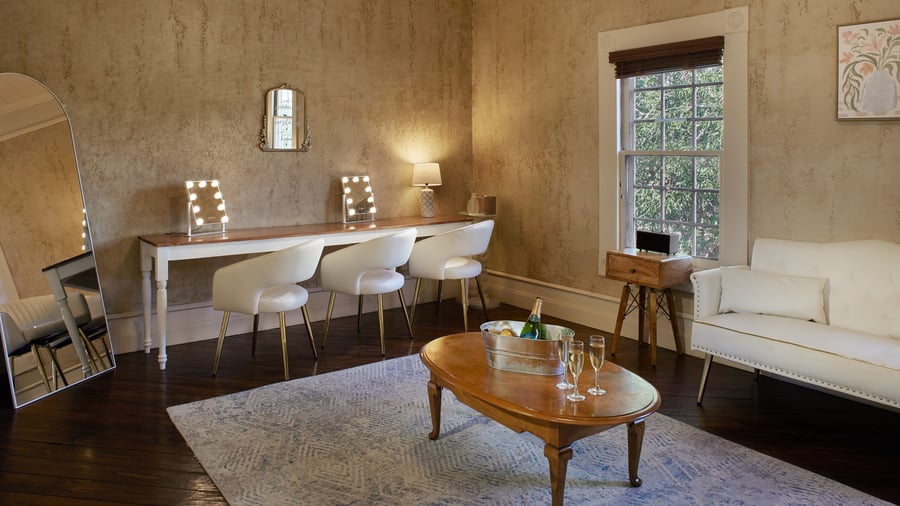 Bridal suite at Hofmann Ranch featuring makeup vanities with lit mirrors, elegant seating, and natural light for wedding preparations.