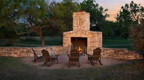 Cozy outdoor stone fireplace at Hofmann Ranch with Adirondack chairs set under the Texas evening sky.