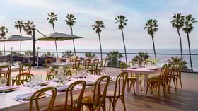 Outdoor dining tables with white linens and palm tree ocean views
