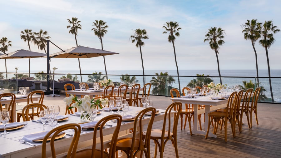 Outdoor dining tables with white linens and palm tree ocean views