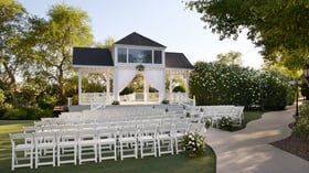 Elegant outdoor wedding ceremony at Lindsay Grove in Mesa, AZ featuring a white gazebo with draped fabric, rows of white chairs, and lush greenery.