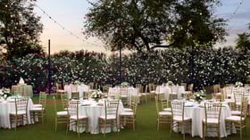 Outdoor evening wedding reception at Lindsay Grove in Mesa, AZ with romantic lighting, round tables, gold chiavari chairs, and floral centerpieces