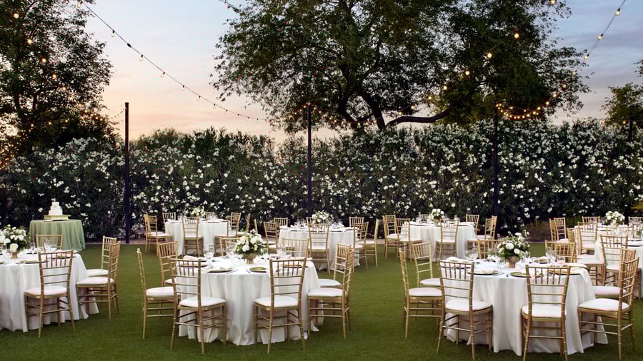 Outdoor evening wedding reception at Lindsay Grove in Mesa, AZ with romantic lighting, round tables, gold chiavari chairs, and floral centerpieces