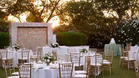 Evening reception at Lindsay Grove in Mesa, AZ with white table linens, gold chiavari chairs, floral centerpieces, and string lights against a sunset backdrop.