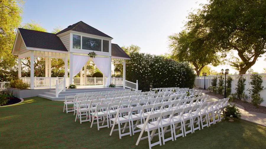 Outdoor gazebo wedding ceremony at Lindsay Grove in Mesa, AZ with white draped fabric, rows of white chairs, and landscaped garden backdrop.