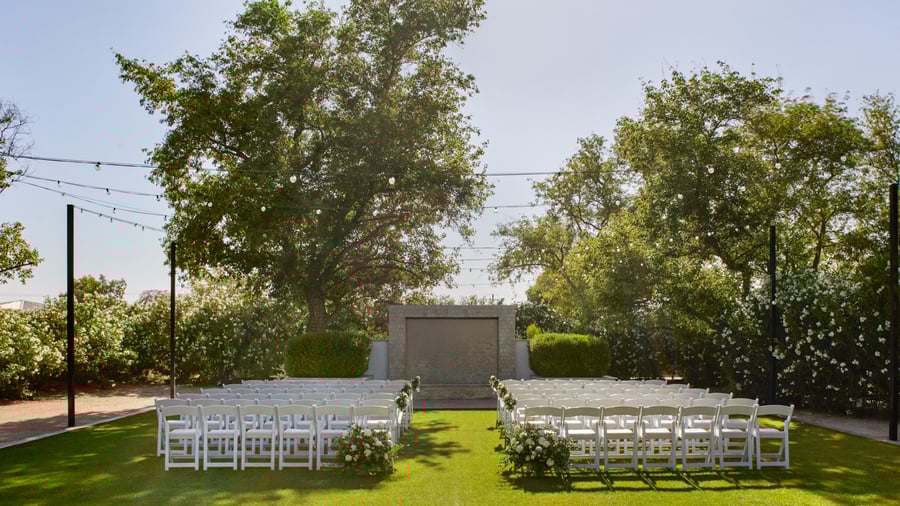 Elegant outdoor ceremony setup at Lindsay Grove in Mesa, AZ featuring a stone wall backdrop, rows of white chairs, and floral accents