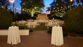 Brick patio cocktail reception at Lindsay Grove in Mesa, AZ with high-top tables, floral accents, and twinkle lights illuminating the garden.