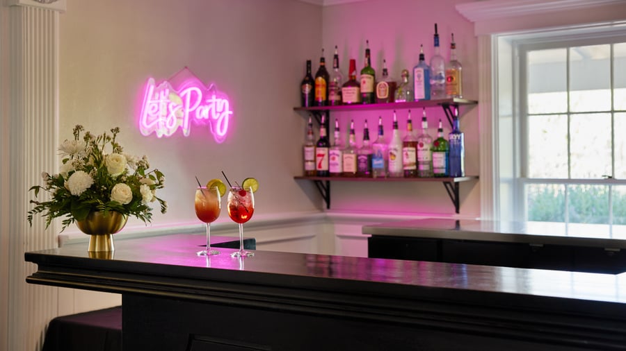 Stylish wedding bar inside Lindsay Grove Grand Hall in Mesa, AZ with a neon “Let’s Party” sign, floral arrangement, and colorful cocktails.