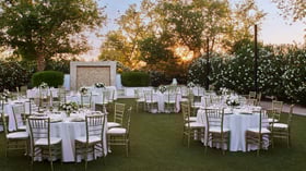 Sunset wedding reception at Lindsay Grove in Mesa, AZ with round tables, gold chiavari chairs, floral centerpieces, and string lights overhead.