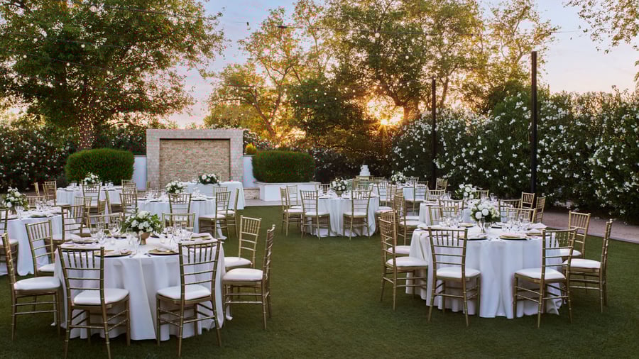Sunset wedding reception at Lindsay Grove in Mesa, AZ with round tables, gold chiavari chairs, floral centerpieces, and string lights overhead.