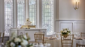 Elegant tiered wedding cake on a gold stand at Lindsay Grove Grand Hall in Mesa, AZ with stained glass windows and floral table décor.