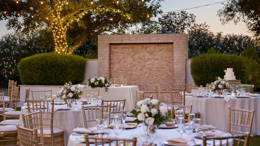 Romantic outdoor reception at Lindsay Grove in Mesa, AZ with round tables, floral centerpieces, gold chairs, and glowing string lights.